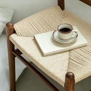 Close‑up view of hand‑woven natural rope seat on solid wood stool with coffee cup and book, wood texture detail