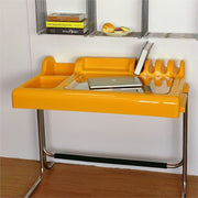 Orange-yellow vanity desk showing recessed organizer zones, glass work surface and chrome frame